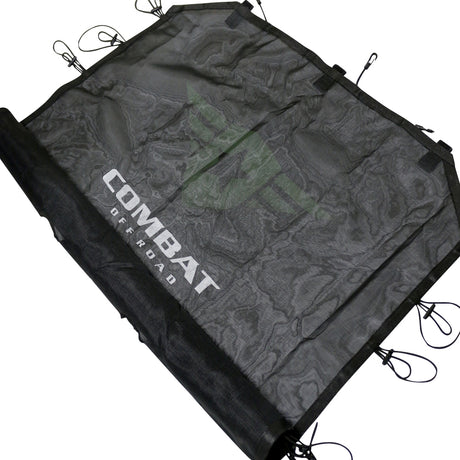Angled view of a black mesh sunshade designed for a 4-door Jeep JK. The Combat Off Road logo is prominently displayed in white across the center of the fabric. The sunshade features durable construction with reinforced edges and multiple bungee cords with hooks around the perimeter, ensuring a secure fit to the vehicle's roll bars. The material provides shade while maintaining airflow for a comfortable interior.